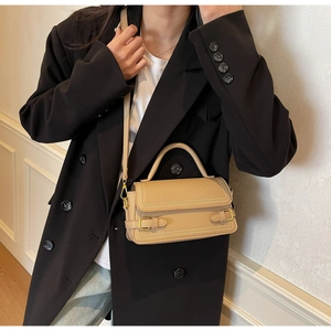 Detail of beige litchi grain leather texture and gold hardware on square handbag