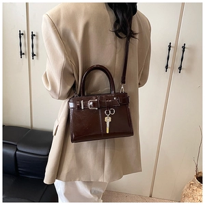 Detail of dark brown glossy leather handbag with gold key charm and strap buckle