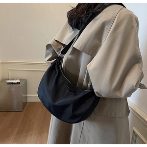 Close-up of black nylon half-moon shoulder bag with pleated texture on model's outfit