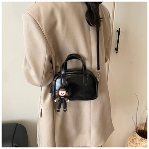 Details der schwarzen glänzenden Boston-Tasche mit Puppenanhänger und schmalem Schultergurt