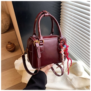 Detail of burgundy Boston bag with white stitching, dual handles and woven rope charm