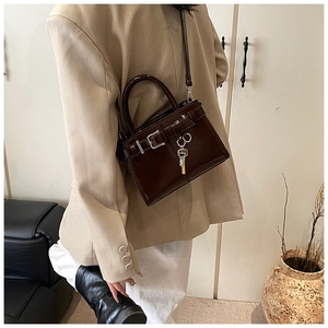 Detail of dark brown patent leather handbag with buckle strap and key-shaped metal charm