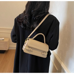 Rear view of a beige pebble leather handbag with gold buckles and adjustable strap