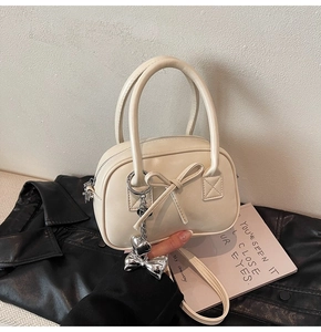Dettaglio di una borsa bowling crema con decorazione a fiocco e ciondolo a cuore