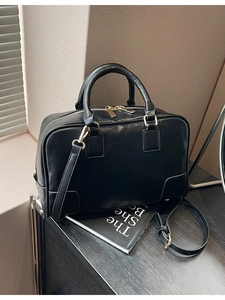 Minimalist black Boston handbag with gold hardware shown under shutter shadows