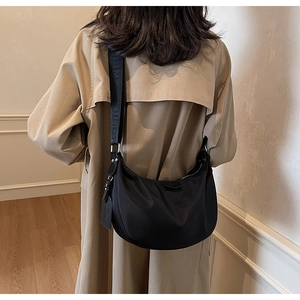 Detailed back view of a black crescent crossbody bag worn over a trench coat