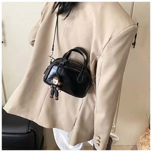 Detail der schwarzen Mini-Kissentasche mit süßem Puppenanhänger auf khaki Blazer