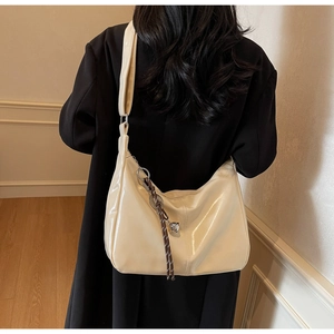 Detail of a large cream crossbody bag with glossy patent texture and stylish charm