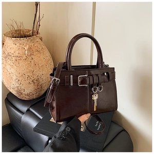 Detail of dark brown leather handbag featuring golden key pendant and strap buckle