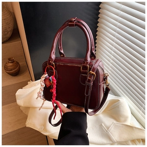 Detail view of deep red Boston bag with white stitching and decorative red-white charm