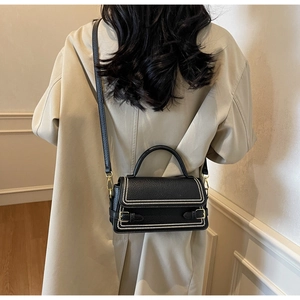Detailed view of black pebbled leather crossbody bag with pearl trim and gold buckles