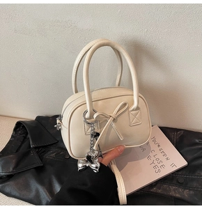 Dettaglio della borsa in ecopelle crema con fiocco decorativo e ciondolo a cuore argento