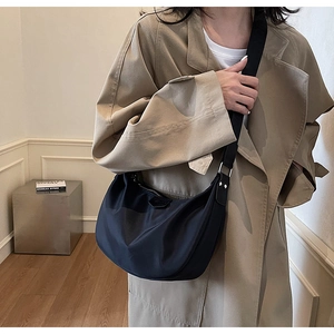 Close-up of a black crescent nylon shoulder bag with wide strap on a khaki coat
