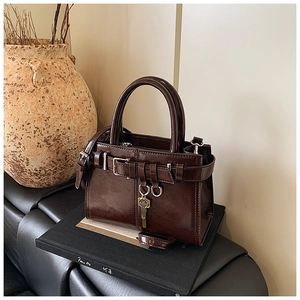 Detail of dark brown faux leather handbag with metal buckle and vintage key charm