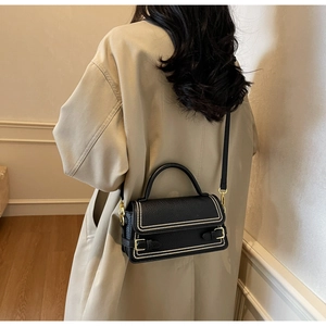 Detail of black pebbled leather crossbody bag with gold rivets worn on trench coat