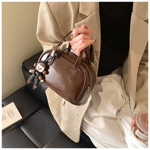 Detailansicht einer dunkelbraunen Vintage-Henkeltasche mit Anhänger und Reißverschluss