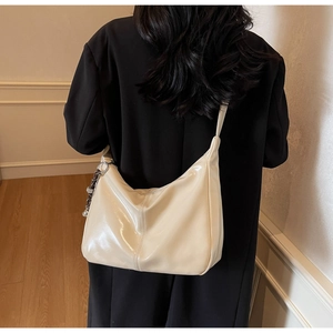 Detail of glossy beige leather hobo bag with metal ring zipper and woven charm strap