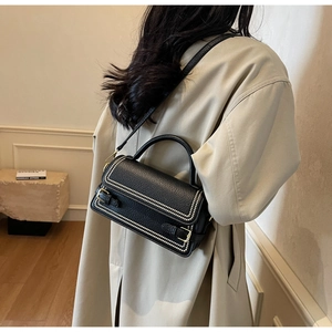 Detail view of black pebble leather handbag with white stud trim and gold buckles on a model