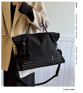 Detail of black tote bag with silver metal rivets on base and decorative side tassel charm