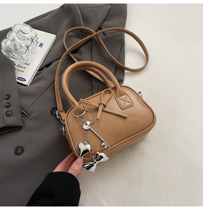 Dettaglio borsa bowling marrone con ciondoli metallici e fiocco su sfondo blazer grigio