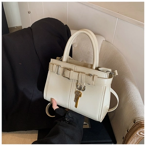 Detail of cream leather handbag with gold key pendant and decorative buckle strap