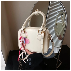 Detailed close-up of cream Boston bag with gold rings and decorative floral pendant charm