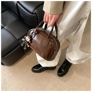 Detailansicht einer dunkelbraunen Boston-Handtasche mit süßem Anhänger und Metallreißverschluss