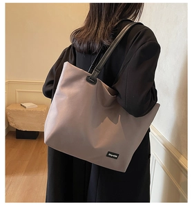 Vue de dos d'un modèle portant un grand sac cabas en nylon gris-mauve aux anses en cuir