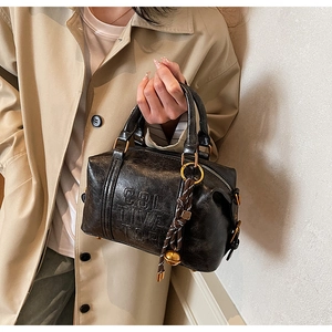 Detail of black wax leather handbag featuring gold hardware and stylish woven charm