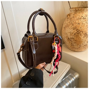 Close-up of brown Boston bag showing contrast stitching and colorful braided charm
