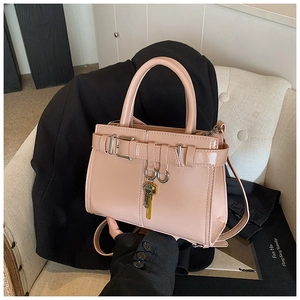 Detail of pink faux leather handbag with golden key charm and top handle on a white chair