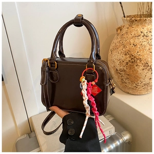 Detail of dark brown leather Boston bag with white stitching and colorful woven charm