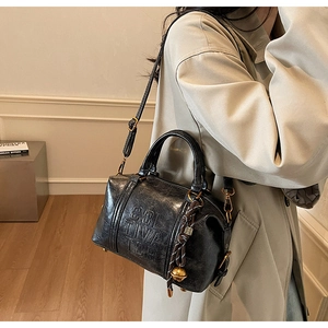 Macro view of black leather Boston bag featuring SOL TIVA TOR embossing and bell charm