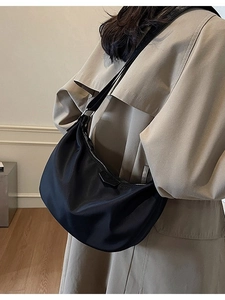 Chic black nylon crescent dumpling bag with adjustable strap worn with a beige trench coat