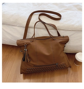 Close-up of vintage brown tote bag with metal rivets, side tassels, and zipper detail