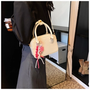 Model wearing a cream white Boston handbag with a lucky charm woven accessory