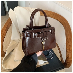 Detail of chocolate brown patent leather handbag with silver buckle and key charm