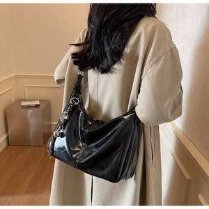 Detail of glossy black faux leather tote with silver buckle and decorative tassel charm