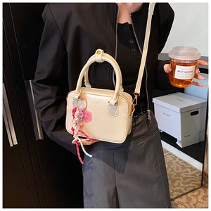 Detail of a beige Boston bag with floral charm and adjustable strap held by a model