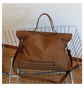 Close-up of brown matte tote bag with metal rivet studs and leather tassel in a cart