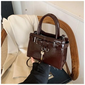 Close-up of deep burgundy patent leather handbag with gold key charm on a wooden chair