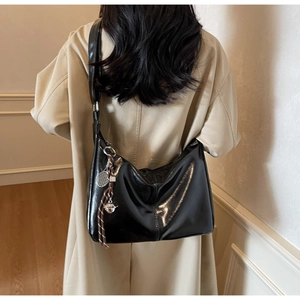 Detail of a black glossy hobo bag with a tennis racket charm on a khaki trench coat