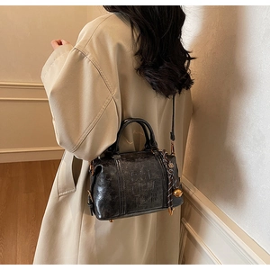 Close-up of vintage black crossbody bag with embossed letters and bell charm detail