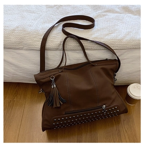 Close-up of brown tote bag featuring decorative leather tassels and metal rivet details