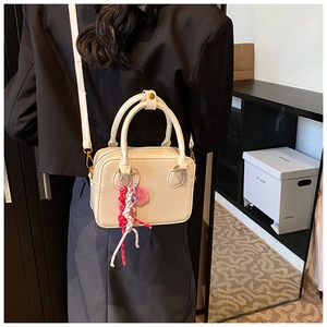 Detail of a beige small bowling bag showing the woven charm and adjustable crossbody strap