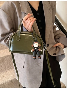 Dunkelgrüne Leder-Boston-Tasche mit Anhänger und Schultergurt auf einer Treppe gezeigt