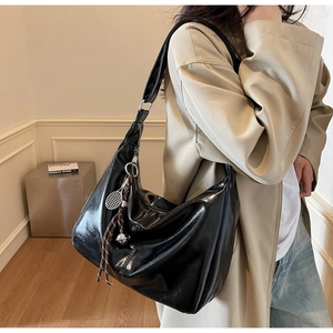 Detail of black glossy leather hobo bag with a silver tennis racket charm accessory