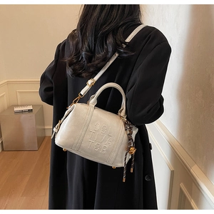 Detailed close-up of cream Boston bag with embossed letters and woven pendant detail