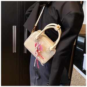 Detail of cream white leather bowling bag with cute pendant held by model in black blazer
