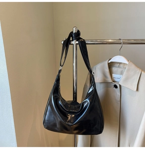 Detail of glossy black crescent shoulder bag with silver zipper on a metal hanger